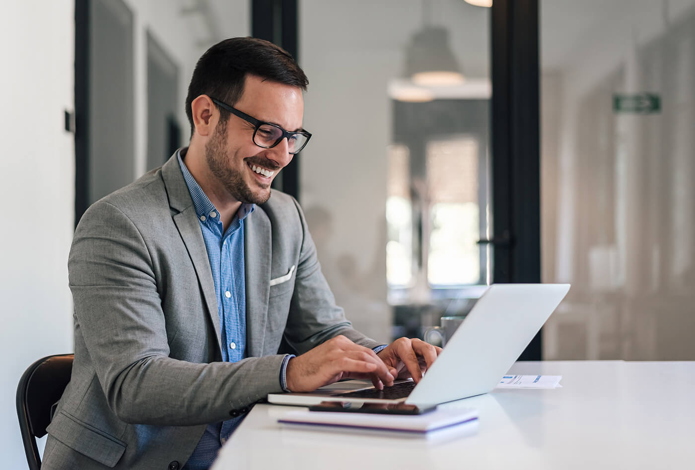 Smiling man in glasses with replacement occupational lenses works on laptop in office